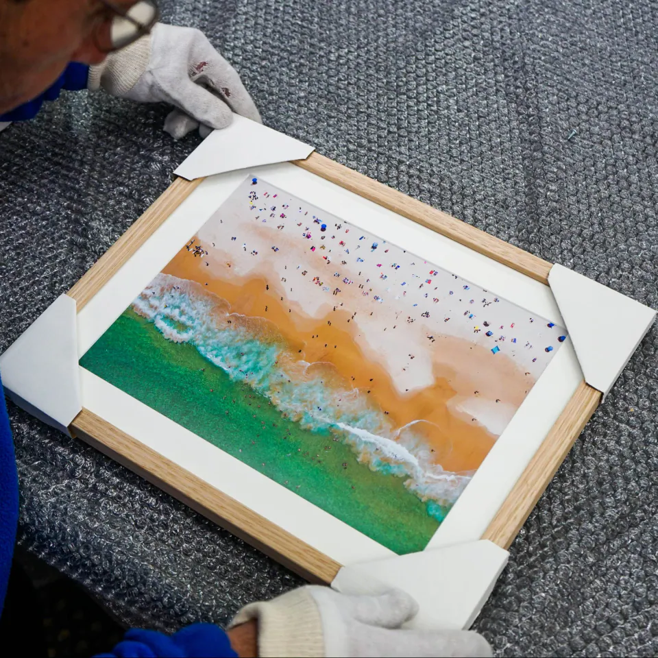 A Frameshop framer finishing a custom framed beach photograph in the workshop