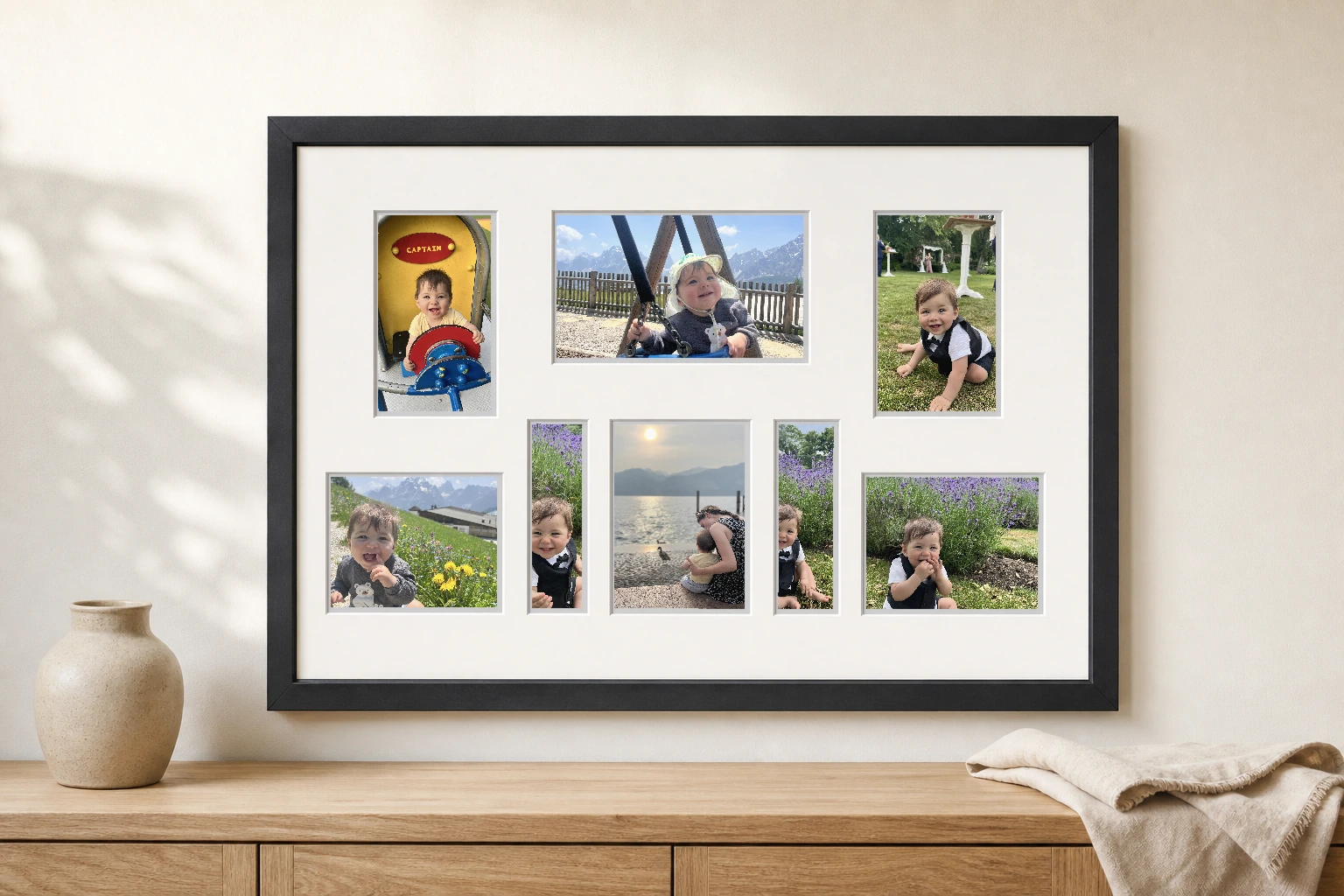 Black eight-opening collage frame displaying a baby's first-year and family adventure photographs above a timber console