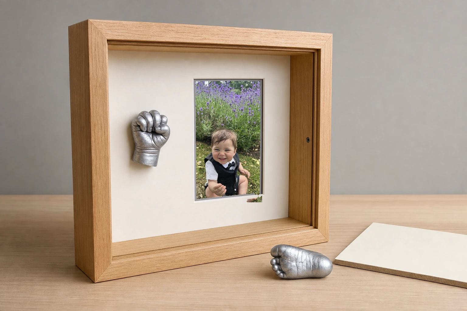 Open natural oak shadow box with a baby portrait and mounted hand casting beside a loose foot casting and backing board